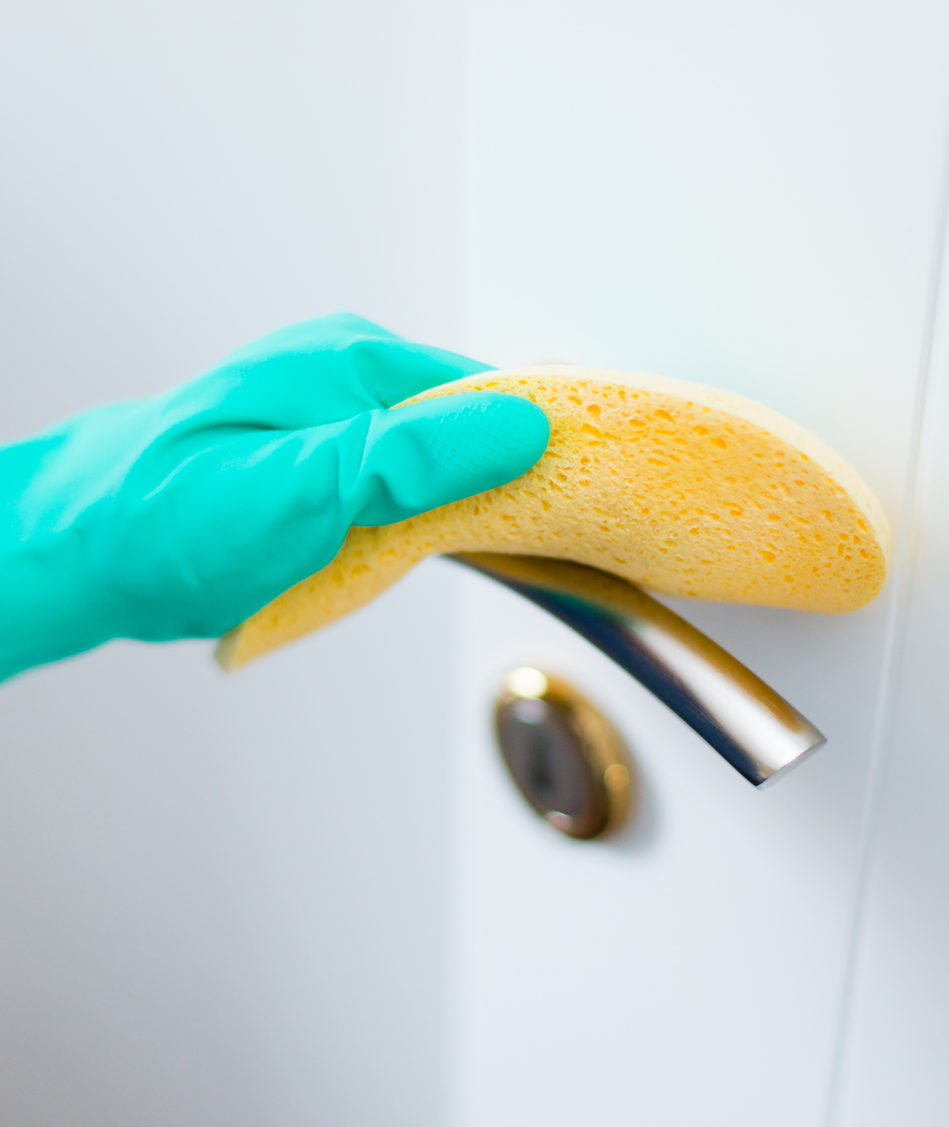 Hand in rubber glove sanitizing a door handle with yellow sponge